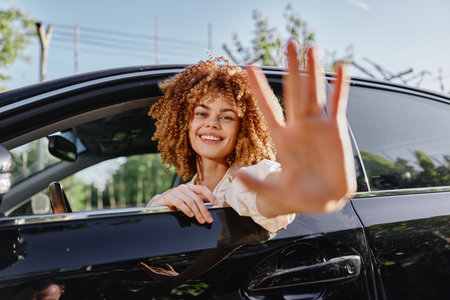 smiling woman with curly hair sitting in black car holding hand out, natural light, casual outfit, outdoor setting, happy expression, summer dayの写真素材
