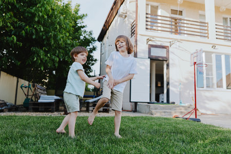 Two cheerful boys playing together in a sunny backyard, enjoying their time outdoors on a warm day, showcasing laughter and friendship in a joyful setting.の写真素材