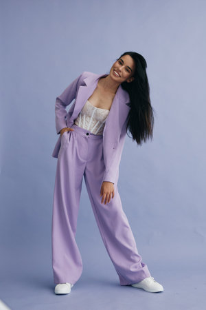 Young woman wearing lilac pantsuit and white sneakers posing stylishly against a soft purple background, showing modern fashion and relaxed confident attitude.の写真素材