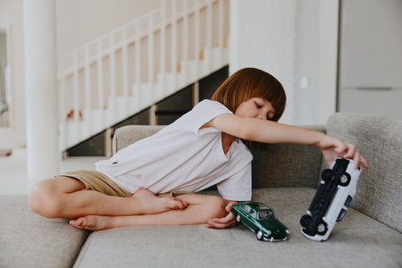 Playful boy engaging with toy cars on a cozy sofa, showcasing creativity and imagination during playtime. Bright indoor setting emphasizes a joyful atmosphere.の写真素材