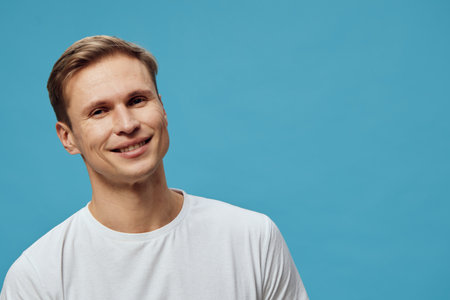 Smiling man with short brown hair wearing casual white t-shirt, looking at camera, standing against...