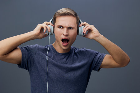 surprised young man listening music with headphones on dark gray background expression emotion...