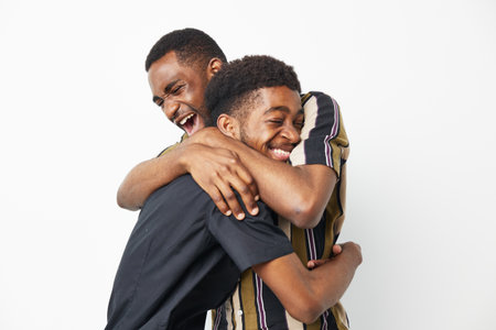 Two joyful African American men share a warm embrace, showcasing happiness and friendship. Their...