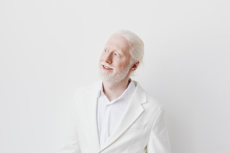 Smiling man with light blonde hair and beard wearing a white suit against a plain white background, conveying positivity and confidence Ideal for portraying elegance and sophisticationの写真素材