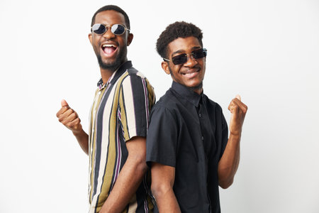 Two cheerful African American men wearing sunglasses and stylish shirts pose in a dynamic way, showcasing their playful friendship and vibrant personality.の写真素材
