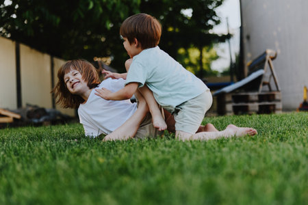 Happy children playing together on a grassy lawn, enjoying the sunlight and bonding through laughter and fun. Perfect for portraying childhood joy and friendship.の写真素材