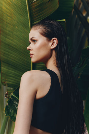 Woman in black top standing in front of palm trees with back to camera, tropical summer vacation conceptの写真素材