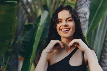 Happy woman in black swimsuit smiling in front of palm trees on tropical beach vacation resortの写真素材
