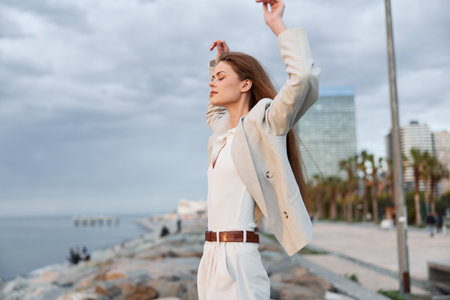 Confident businesswoman in a light suit poses by the seaside, showcasing determination and empowerment against a cloudy sky.の写真素材