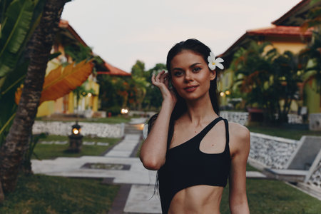 Beautiful woman in black bikini top and flower in hair posing for the camera on the beachの写真素材