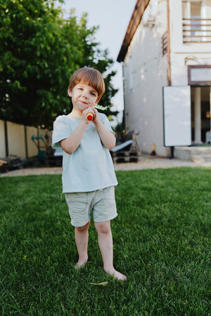 Happy boy holding a carrot, enjoying a sunny day outdoors in a lush green backyard with a playful atmosphere and a carefree spirit.の写真素材
