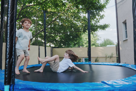 Playful boys enjoying a sunny day on a trampoline in a backyard, showcasing joy and energy while having fun outdoors with friends.の写真素材