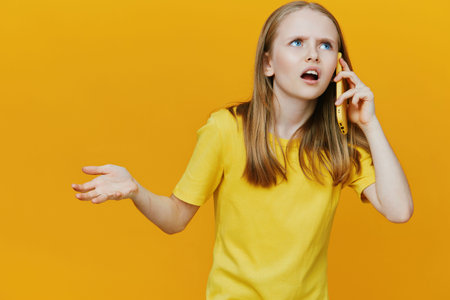 Frustrated girl speaking on the phone against a vibrant yellow background in a casual yellow t...