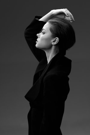 black and white profile of a woman in black clothing with hand raised, elegant pose, soft lighting, minimalistic background, stylish and graceful portraitの写真素材
