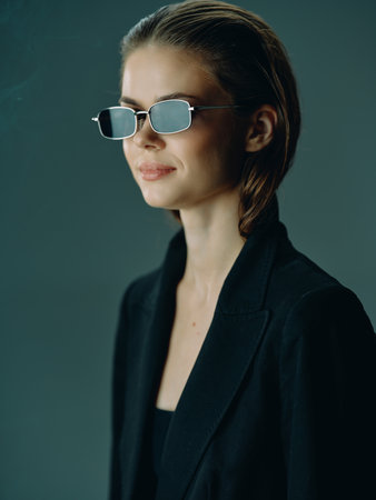 stylish woman wearing sunglasses and black jacket with sleek hairstyle looking away confidently on...