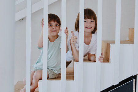 Happy children playing on the stairs, showing joy and excitement in a bright, modern interior, perfect for family-oriented themes and childhood memories.の写真素材
