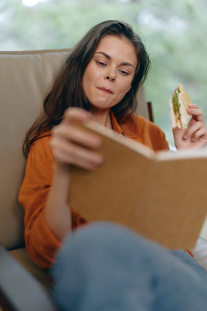 Young woman enjoying a healthy sandwich while reading a book, showcasing a relaxed atmosphere with...