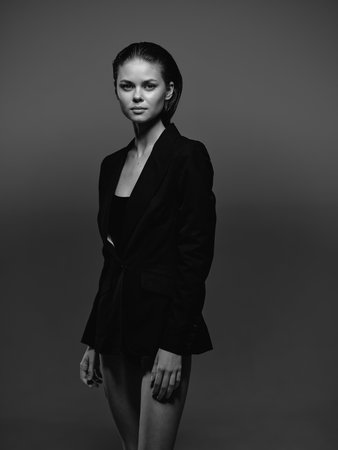 Black and white portrait of a serious woman wearing a dark blazer with natural makeup and slicked-back hair against a simple gray background in studio lighting.の写真素材