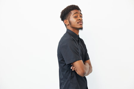 Confident young black man with arms crossed, showcasing a modern black shirt against a minimalist...