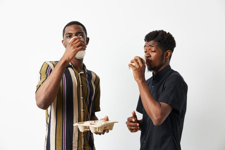 Two young African American men enjoying drinks together, showcasing friendship and joy. They wear stylish outfits and share a light-hearted moment, creating a vibrant atmosphere.の写真素材