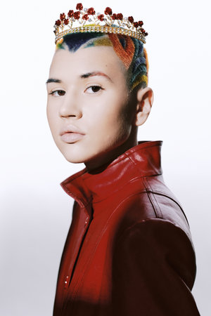 Young woman with colorful shaved hair and golden crown wearing a red leather jacket, confidently posing against white background in contemporary fashion style.の写真素材