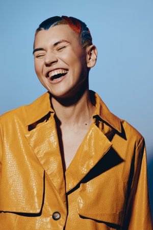 laughing woman with colorful short hair wearing a vibrant yellow jacket, expressing joy and energy...