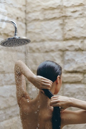 woman showering in outdoor bathroom with stone wall, wet hair, natural light, relaxing self-care moment, wellness and hygiene routineの写真素材