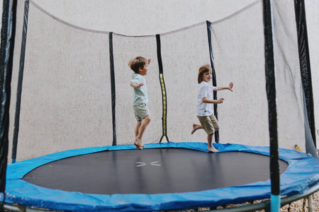 Joyful children bouncing on a trampoline, experiencing fun and excitement. This energetic moment captures playful smiles and joyful movement in a vibrant outdoor setting.の写真素材