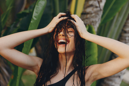 Portrait of a woman with wet hair standing in front of a palm tree with hands on head on tropical beachの写真素材
