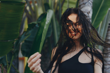 Beautiful woman with long black hair standing in front of a palm tree with her hair blowing in the windの写真素材