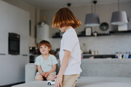 Curious boy playing with a toy car and a friend. Bright living room atmosphere with modern decor, showcasing playful childhood moments and creativity.の写真素材