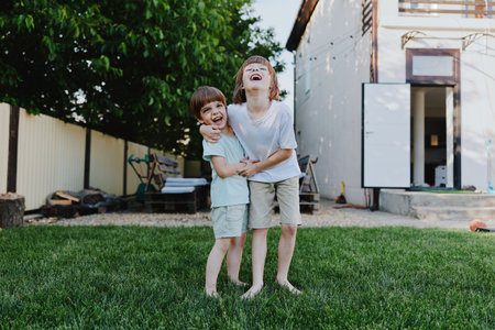 Two joyful boys smiling in a green yard, enjoying a sunny day. Their laughter reflects carefree childhood moments filled with happiness and playfulness.の写真素材