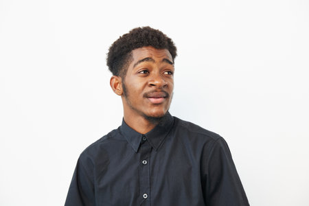 A thoughtful black man with an expressive face, wearing a black shirt against a clean white background, radiating confidence and curiosity in his gaze.の写真素材