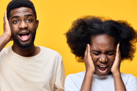 Two diverse people expressing frustration with loud noise, wearing casual clothing against a bright yellow background, capturing emotion and modern styleの写真素材
