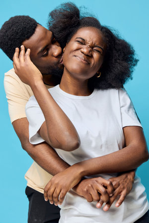 Happy couple enjoying an intimate moment together against a vibrant blue background, showcasing love, joy, and playful emotions in casual clothingの写真素材