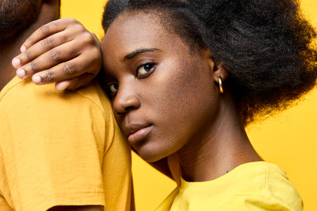Portrait of a young Black woman with natural hair in yellow attire, conveying emotion against a vibrant yellow background, showcasing connection and warmthの写真素材
