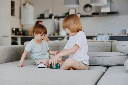 Two boys playing with toy cars on a cozy sofa in a modern living room, showcasing creativity and fun in a bright and welcoming environment.の写真素材