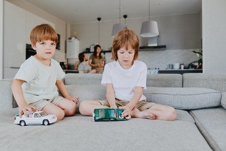 Two young boys playing with toy cars in a cozy living room, showcasing a warm family atmosphere. The scene is inviting and filled with joy and imagination.の写真素材