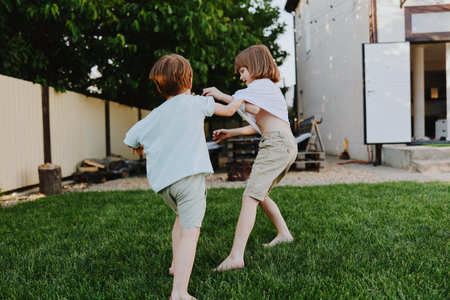 Two playful children running in the garden, enjoying their carefree summer day, engaged in a joyful...