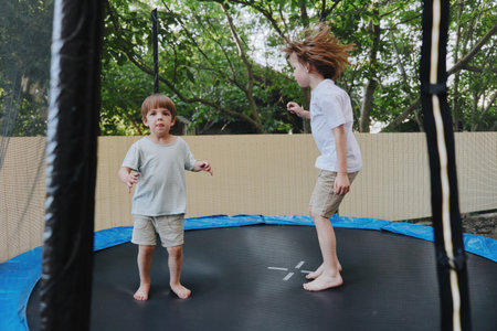 Joyful boys bouncing on a trampoline, enjoying childhood moments under a tree shade, exuding happiness and energy during playful summer days.の写真素材