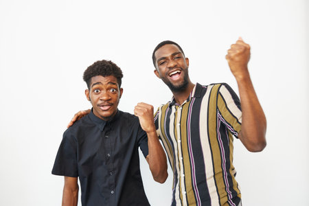 Two happy African American men celebrating together, showing excitement and joy. Their vibrant outfits and cheerful expressions convey a sense of camaraderie and positivity.の写真素材
