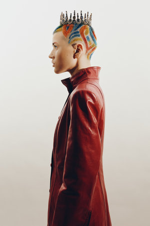 Woman with colorful shaved hair and royal crown wearing a red leather jacket, showcasing bold...