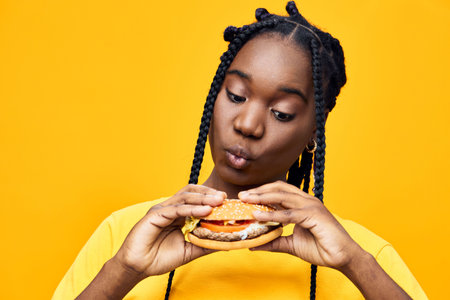 Young Black woman enjoying a delicious hamburger, showcasing excitement and curiosity against a...