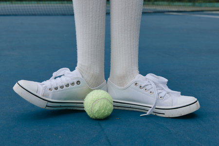 Young athlete with white sneakers standing on a tennis court with a bright green tennis ball, capturing the spirit of sports and energy in a vibrant settingの写真素材