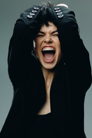 screaming woman with short black hair in black jacket showing intense emotion and frustration on...