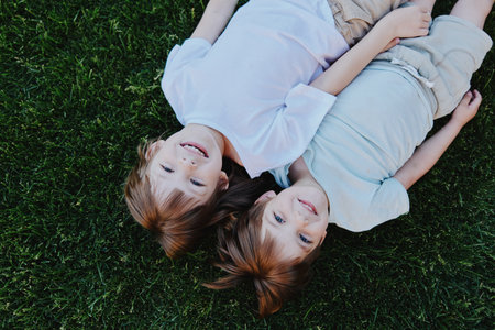 Happy children lying on the grass, enjoying a sunny day, laughing together, carefree moments, friendship, summer joy.の写真素材