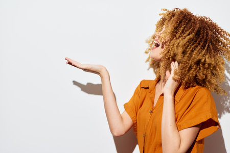 joyful woman with curly hair, expressive pose, orange shirt, white background, smiling and...