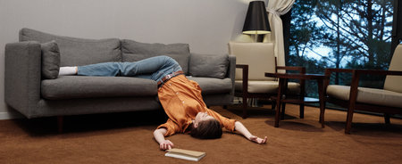 A young woman in casual attire lies exhausted on a sofa, conveying feelings of fatigue and relaxation in a modern indoor setting with warm colorsの写真素材