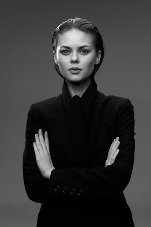 Black and white portrait of a confident woman with crossed arms wearing a dark jacket against a plain studio background, showcasing determination and strength.の写真素材