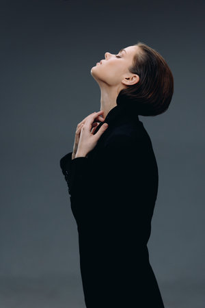 elegant woman in black turtleneck posing with closed eyes and serene expression, dark background, minimalistic style, calm and introspective moodの写真素材